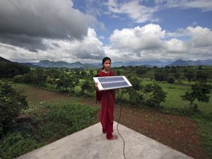 A woman stands outside and holds up a solar panel.