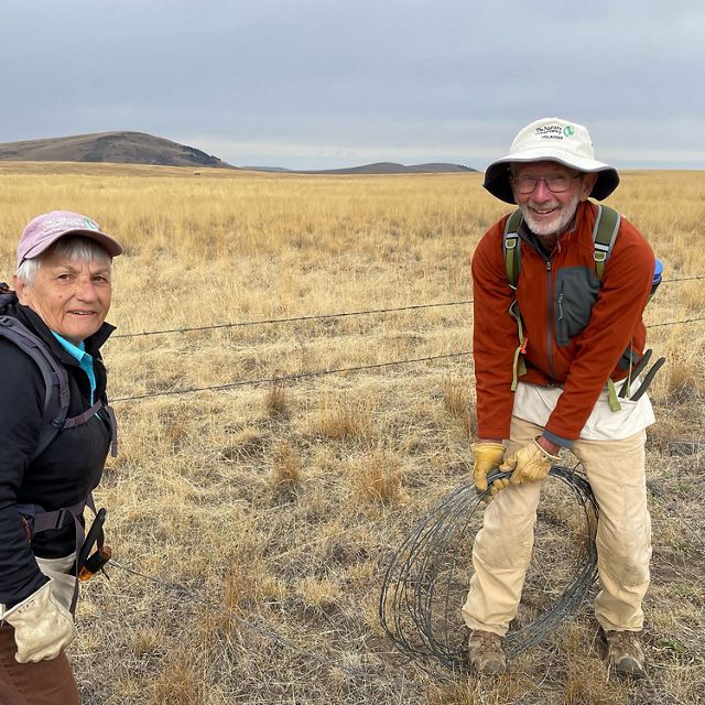 Dale and Lois Derouin stand on an open grassland and remove barbed-wire fencing.