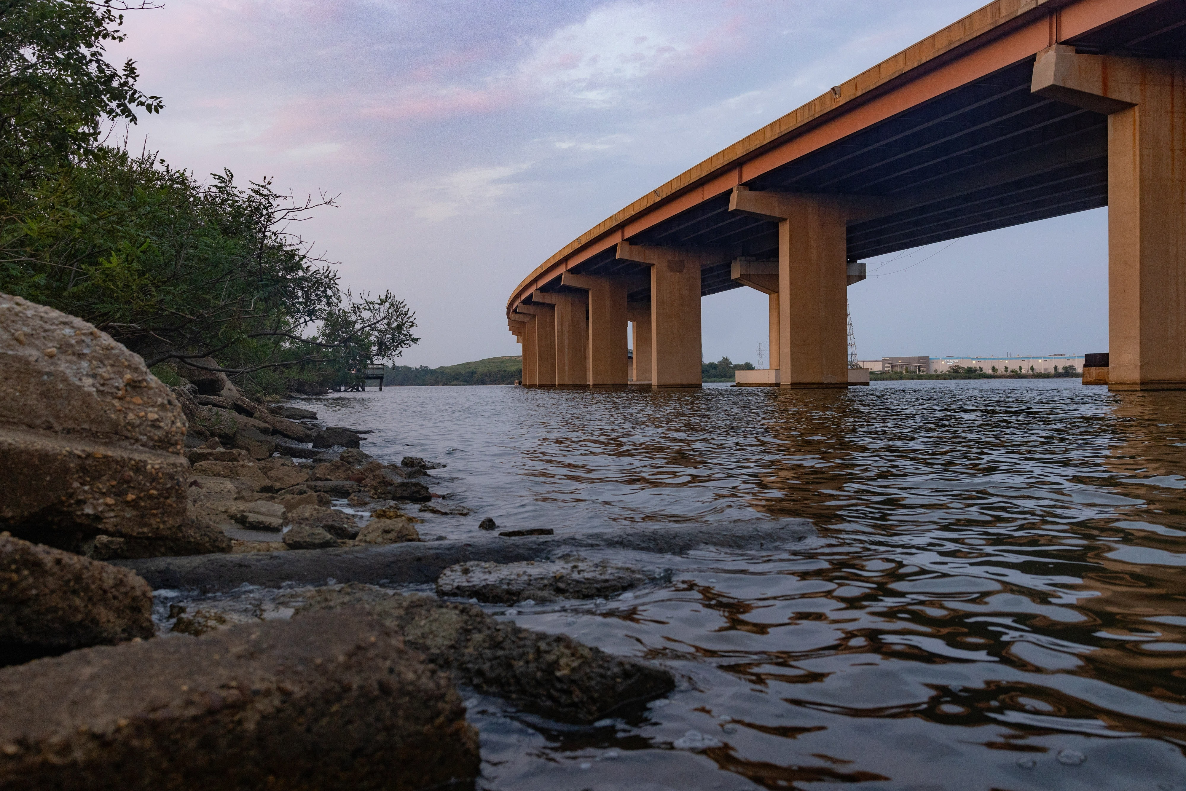 A bridge is seen from a rocky shoreline crossing over a body of water.