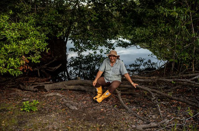 Man poses on a log in front of a lake.