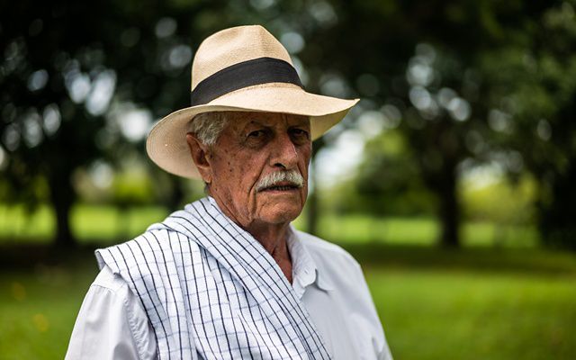An older man with a moustache poses with a straw hat