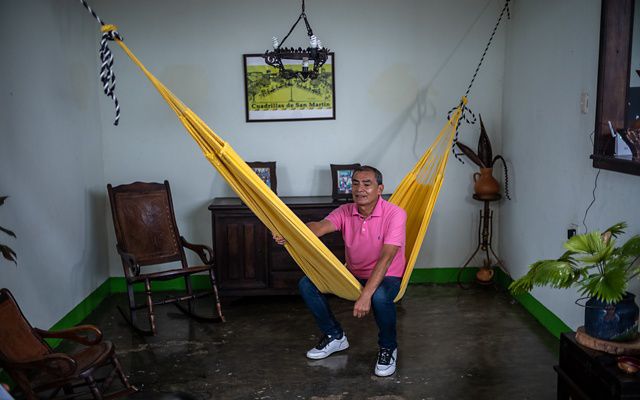 A man in a pink shirt poses on a hammock