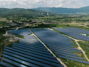 A vast expanse of solar panels in the foreground leads to the base of a now-defunct coal plant in North Macedonia.