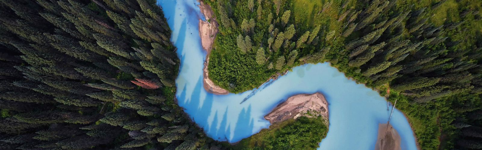 aerial photo of a blue river winding through a forest of evergreen trees.