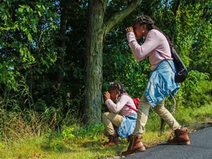 Two young people looking through binoculars into a wooded area.